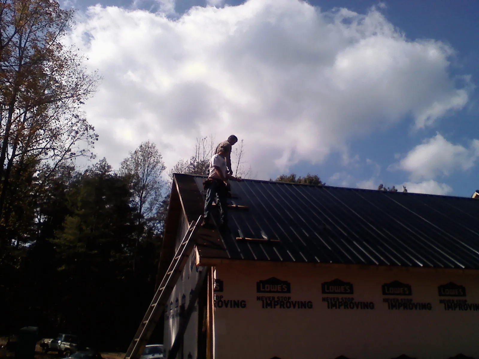 Roofer fastening dark metal panels high against a cloudy sky, from a Roof Inspection job in Beech Island